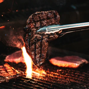 Saftiges Ein Steak wird mit der Grillzange vom Grill hochgehoben auf einem Catering